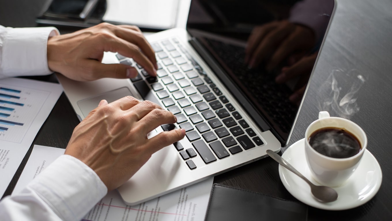focused-professional-typing-on-laptop-with-steaming-coffee-and-charts
